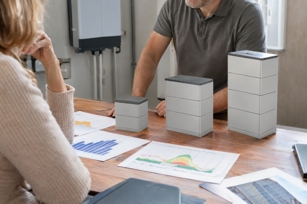 Hausbesitzerin und Fachplaner vergleichen drei Größen eines Batteriespeichers anhand von Energiedaten.